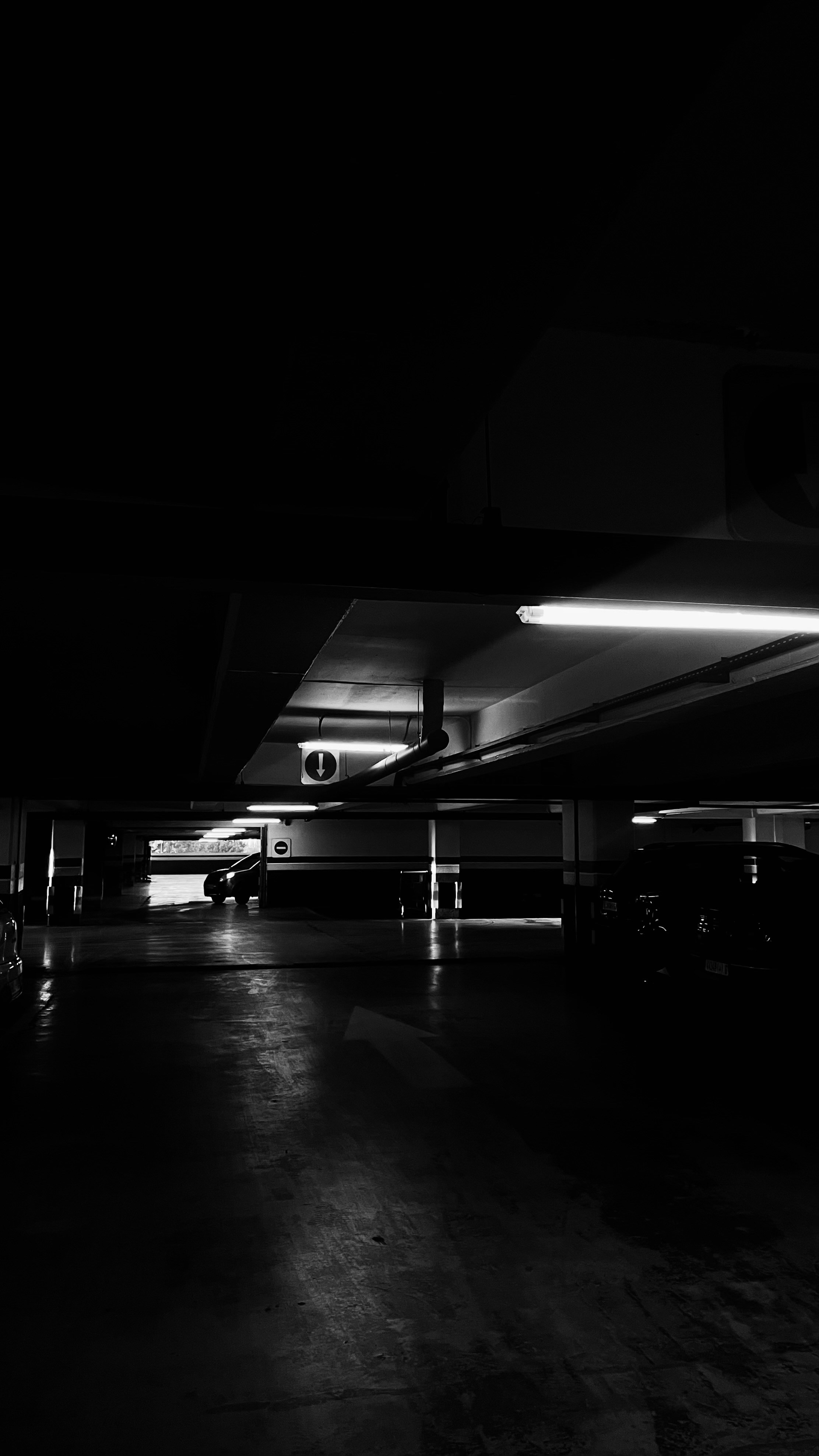 Dark underground parking garage with harsh fluorescent lighting casting sharp shadows, gritty urban atmosphere