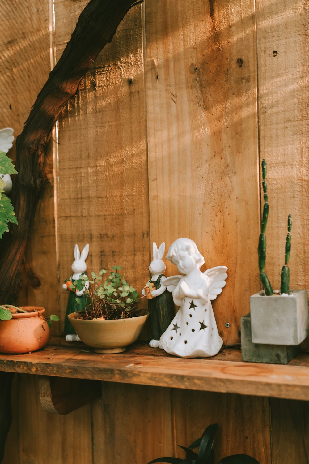 a wooden shelf topped with potted plants and a statue of an angel