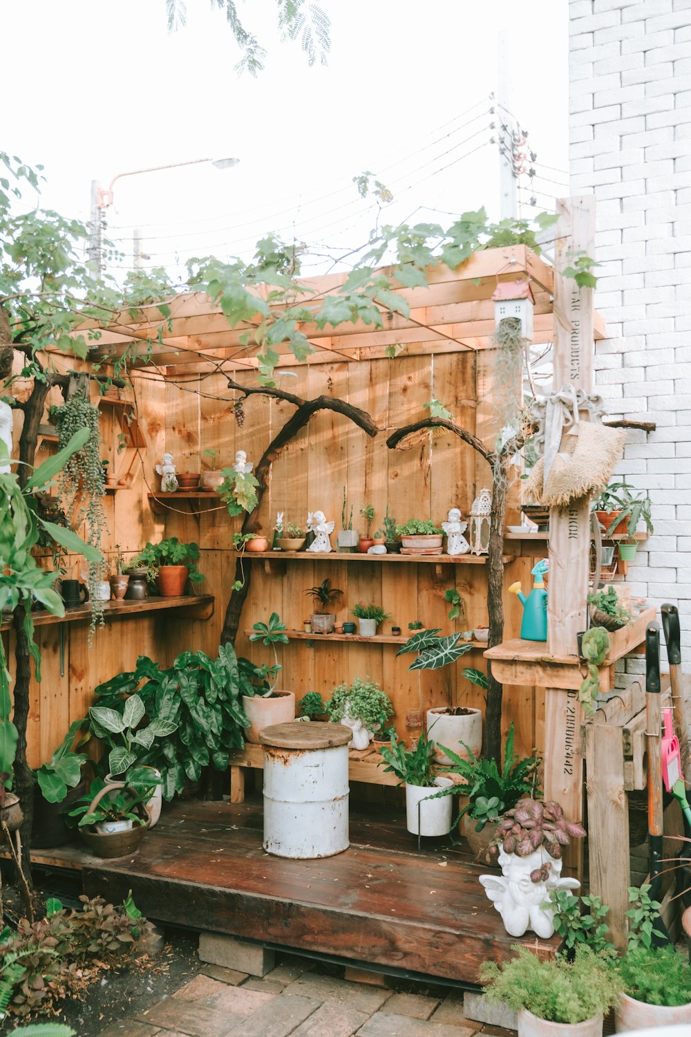 a wooden shelf filled with potted plants next to a brick wall