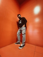 A young person wearing an oversized neon green-accented hoodie standing confidently against a jet black graffiti wall.