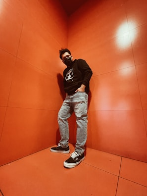 A young person wearing an oversized neon green-accented hoodie standing confidently against a jet black graffiti wall.