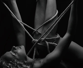 Intricate bondage ropes wrapped artfully around wrists, highlighted by moody blue and black tones.