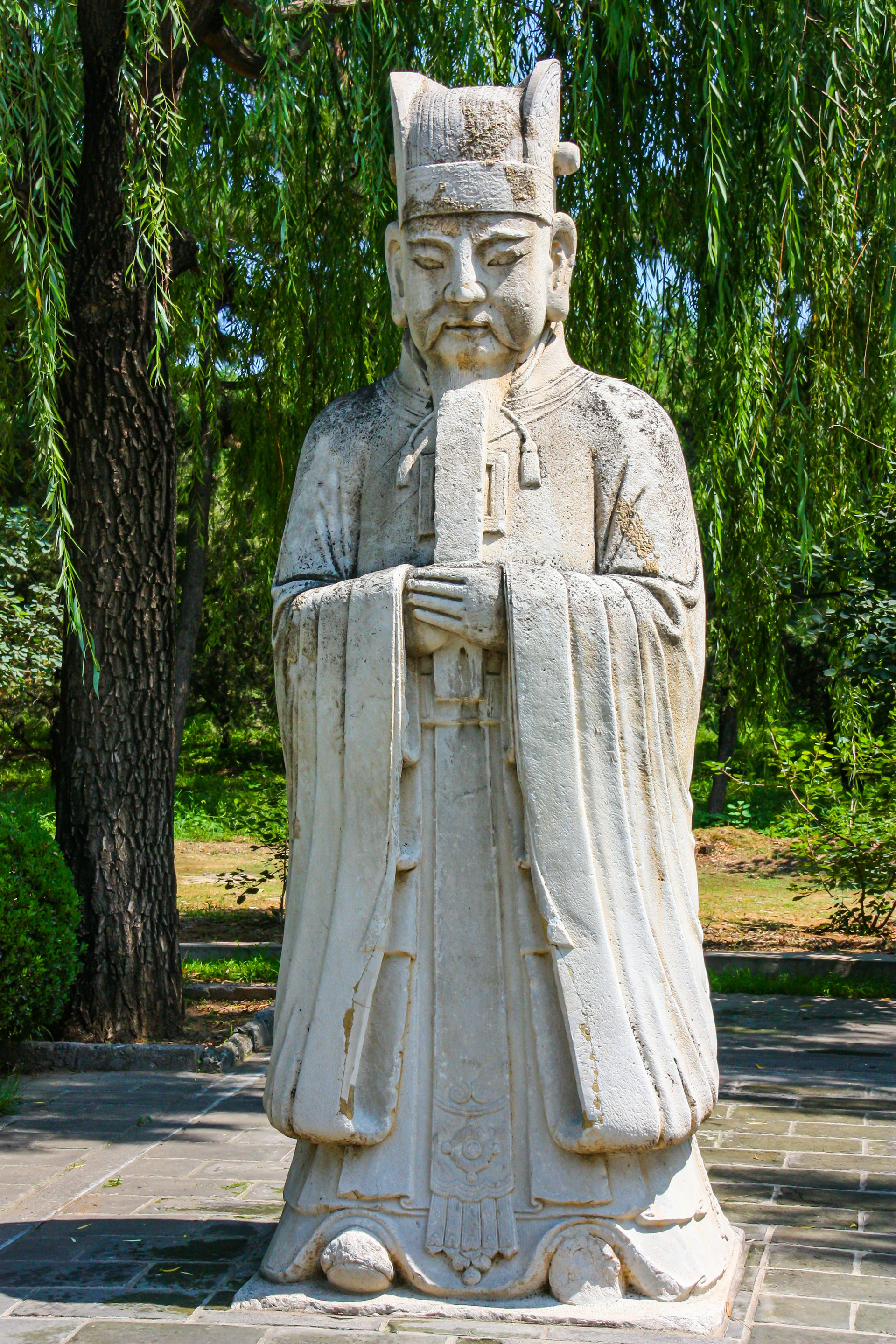 a statue of a man holding a book under a tree