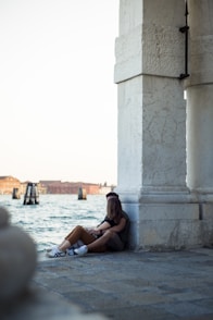a woman sitting on a wall next to a body of water