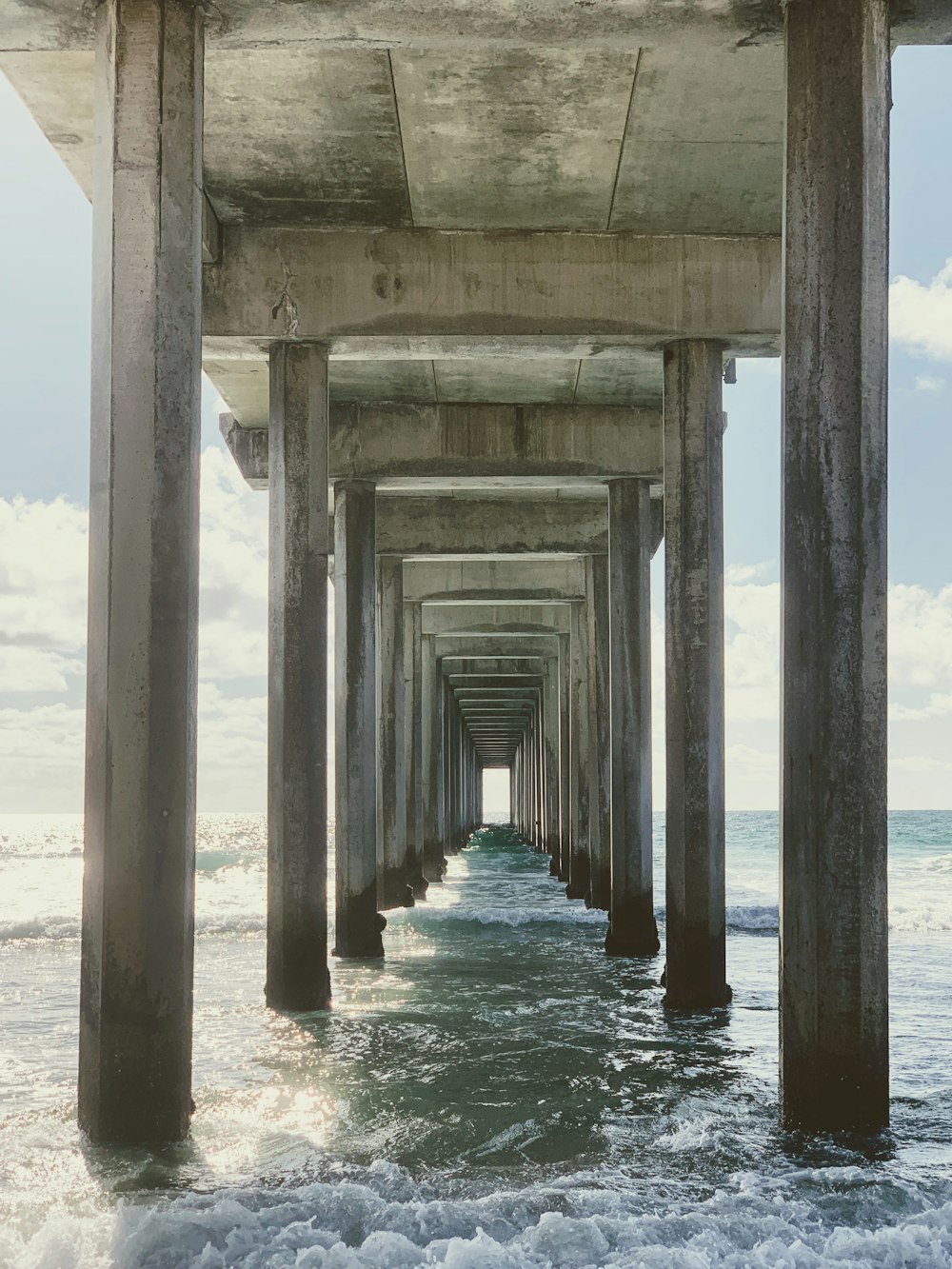 a long pier stretches into the ocean under a cloudy blue sky
