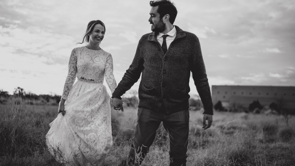 a man and a woman walking through a field holding hands