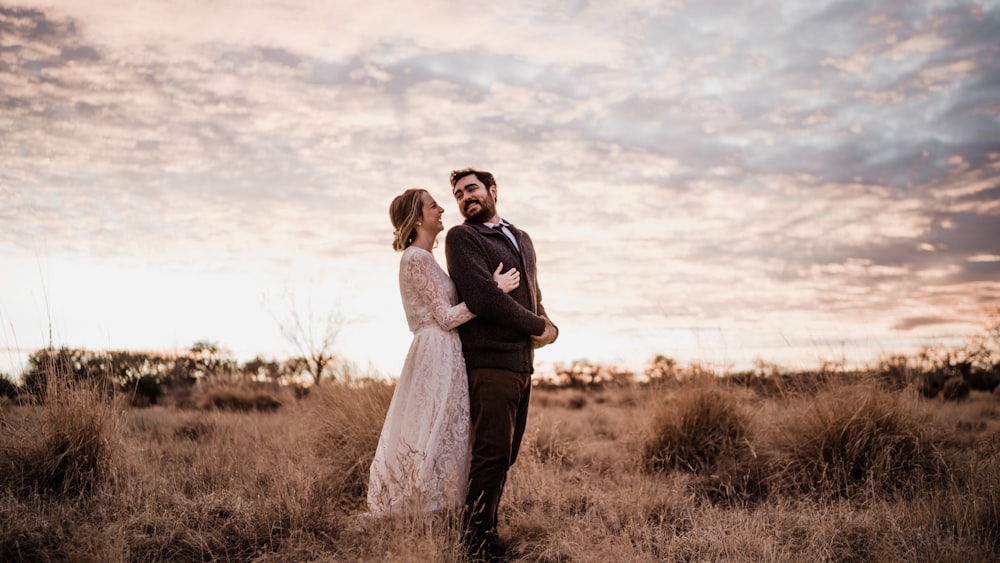 a bride and groom standing in a field at sunset