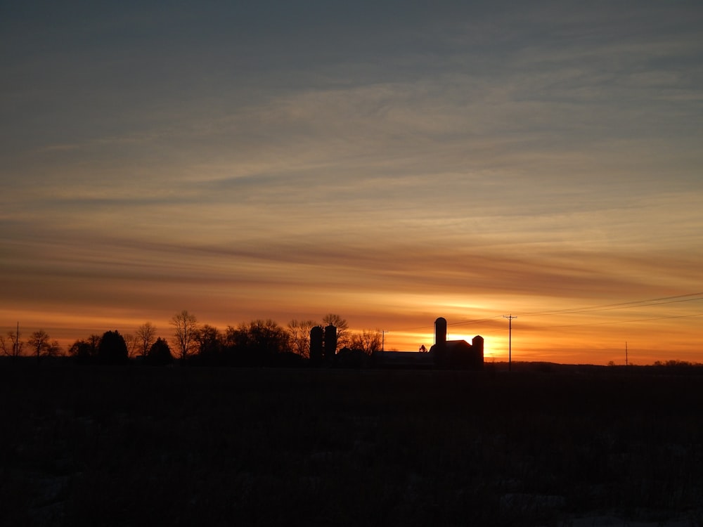 the sun is setting over a farm with silos