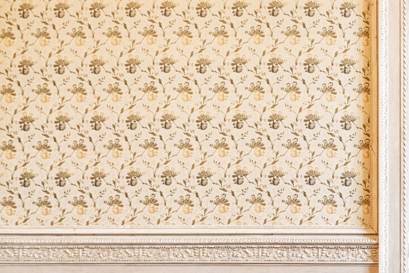 An ornate wall features a vintage floral pattern in muted tones with intricate detailing. The design includes a repeating motif of stylized flowers and vines, bordered by a decorative frame with embossed texture.