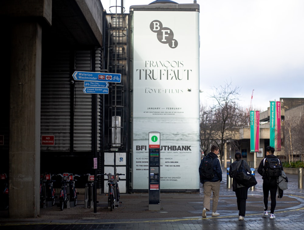 a group of people walking down a street next to a tall sign