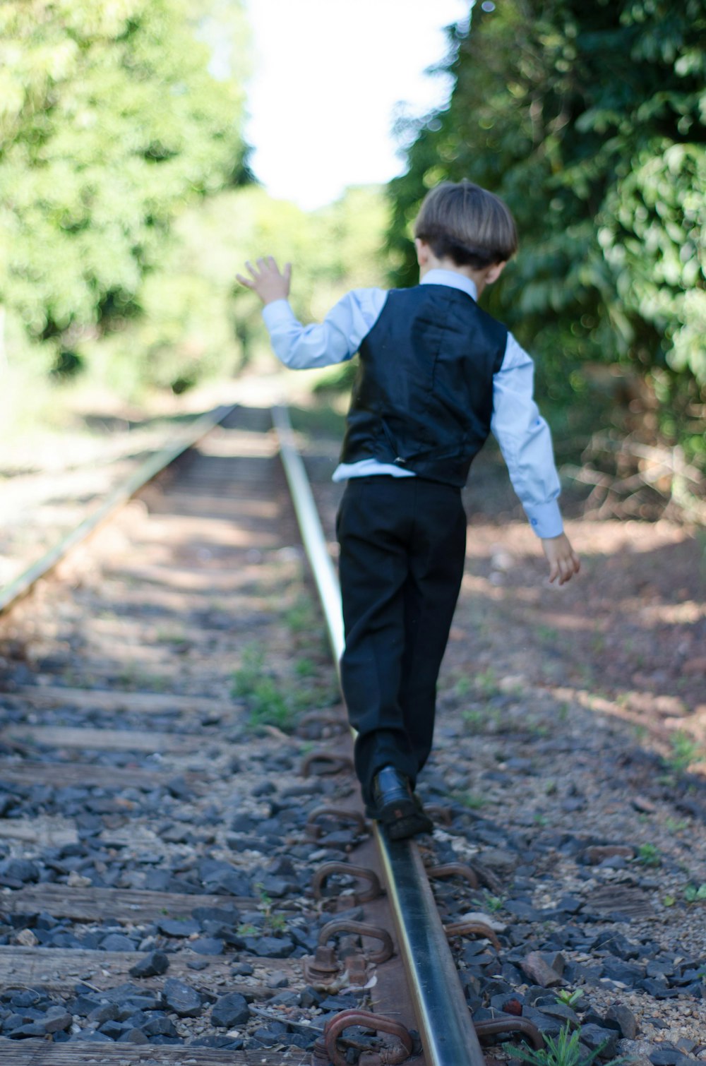 a young boy is walking on a train track