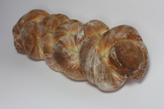 A loaf of bread with a braided shape, covered in a dusting of flour and displaying a golden-brown crust.