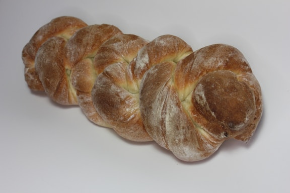 A loaf of bread with a braided shape, covered in a dusting of flour and displaying a golden-brown crust.
