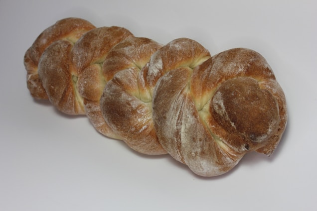 A loaf of bread with a braided shape, covered in a dusting of flour and displaying a golden-brown crust.
