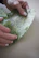 Close-up of hands gently holding a swapped garment in front of a green leafy background.