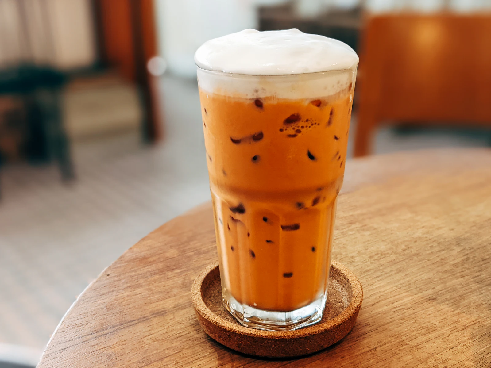 A glass of iced Thai tea with foam on a cork coaster in a quiet cafe