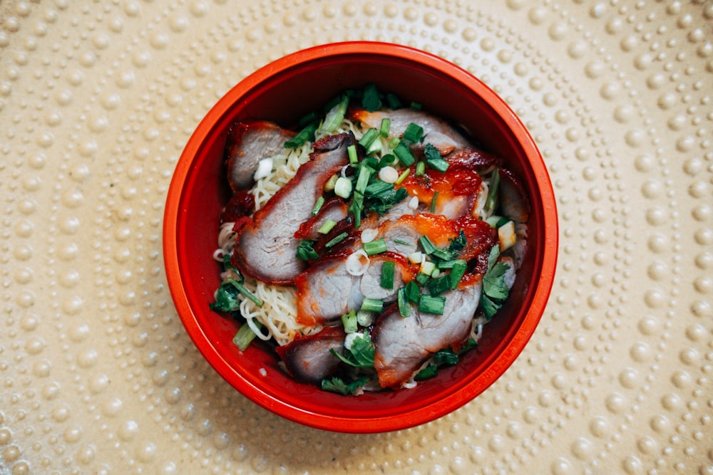a red bowl filled with meat and vegetables