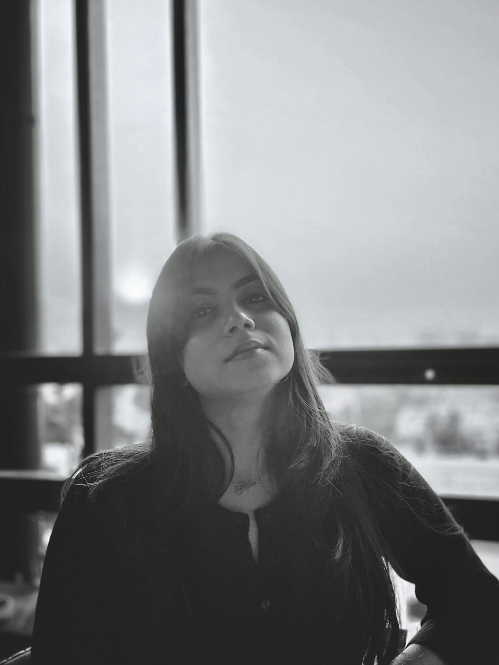 a black and white photo of a woman sitting in front of a window