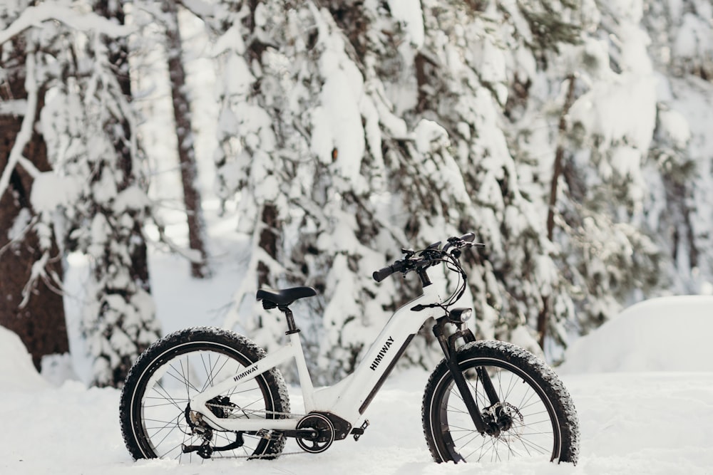 a bicycle parked in the snow in front of trees