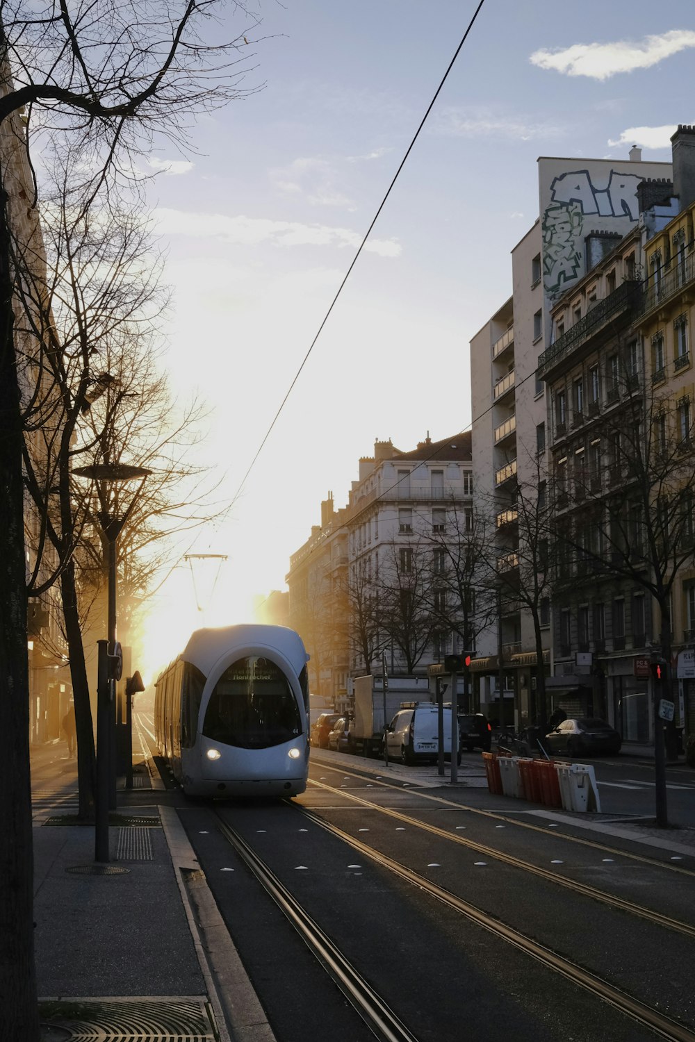 a white train traveling down a street next to tall buildings