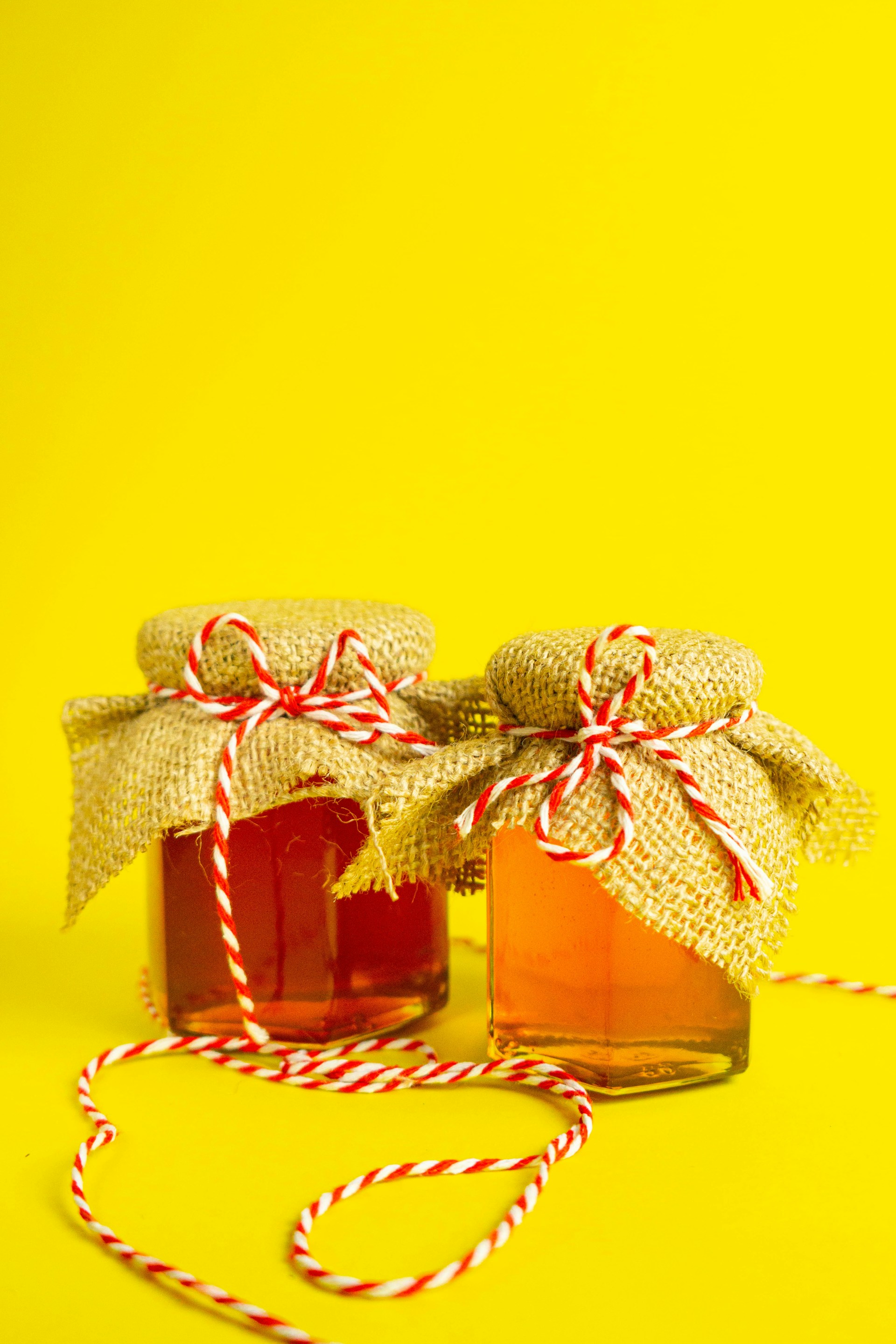 two jars of jam tied with twine on a yellow background