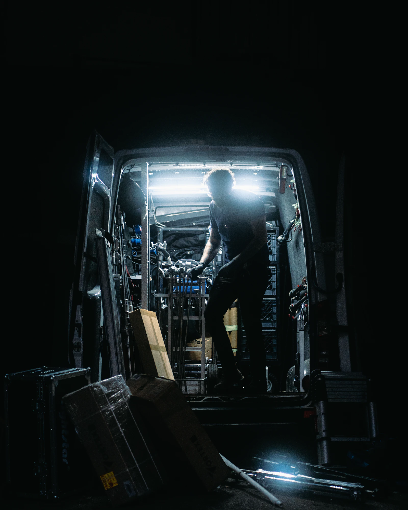 Electrician in a hard hat carrying a tool bag toward a service van at night