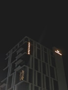A modern high-rise building with illuminated signage displaying the word 'CONCORD' against a dark night sky. The structure features distinct geometric architectural elements and balconies. There is a warm glow emanating from one of the windows, suggesting interior lighting.