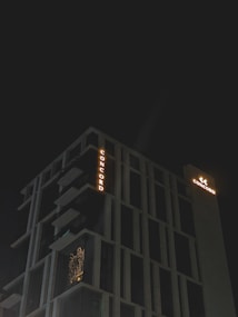 A modern high-rise building with illuminated signage displaying the word 'CONCORD' against a dark night sky. The structure features distinct geometric architectural elements and balconies. There is a warm glow emanating from one of the windows, suggesting interior lighting.