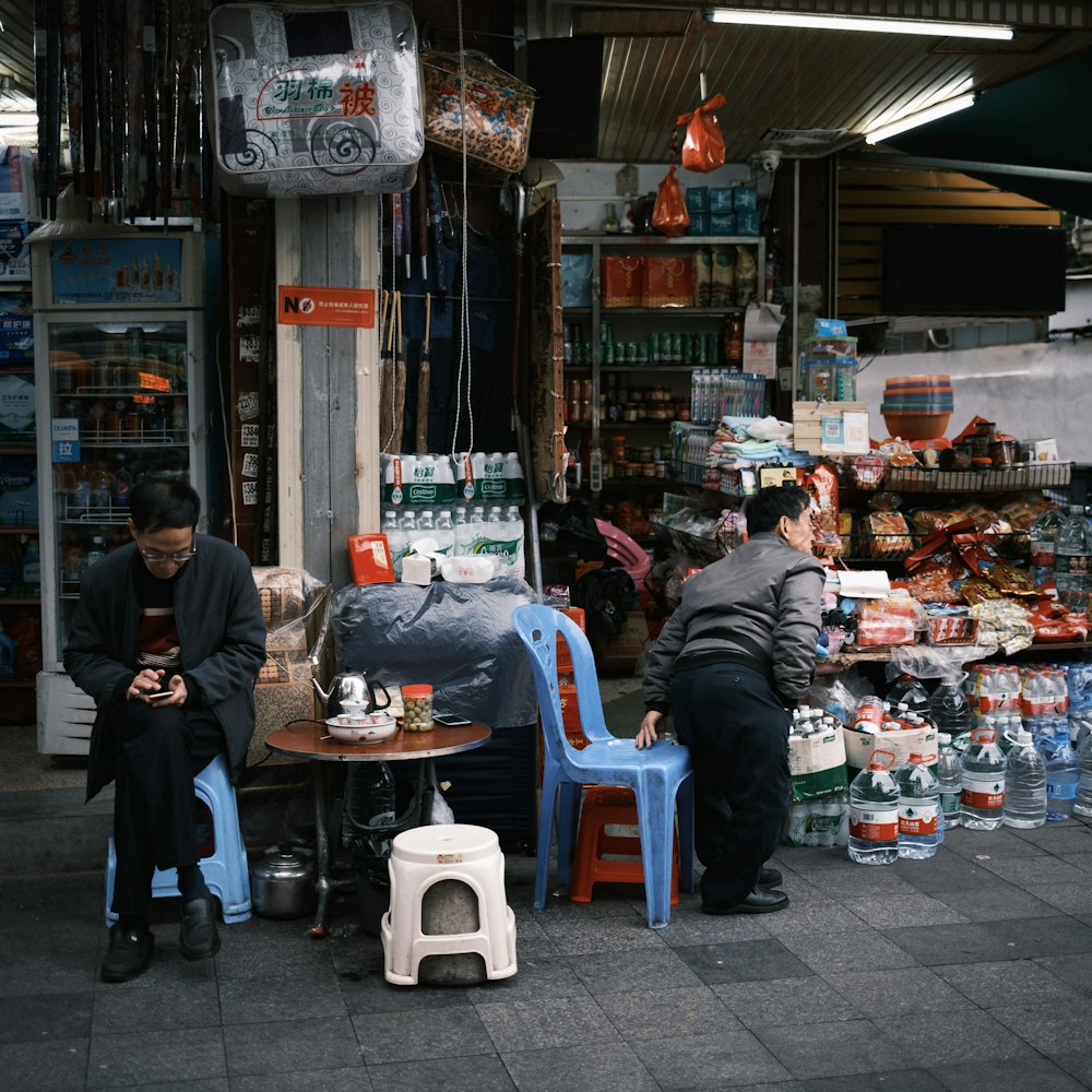 a couple of men sitting at a table in front of a store
