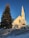 A quaint white church with a tall steeple is set against a clear blue sky. A large pine tree stands to the left of the church. There is snow on the ground, adding to the calm winter atmosphere. The church sign reads 'Casenville United Methodist Church' with an announcement for a potluck following worship.