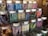 An assortment of glass jars filled with colorful candy sticks, each labeled with different flavors such as blackberry, blueberry, lemon, and licorice. The jars are neatly arranged on wooden shelves in a display that highlights their vibrant hues.