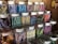 An assortment of glass jars filled with colorful candy sticks, each labeled with different flavors such as blackberry, blueberry, lemon, and licorice. The jars are neatly arranged on wooden shelves in a display that highlights their vibrant hues.