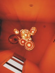 A cluster of hanging pendant lights emits a warm, orange glow, creating an inviting and cozy atmosphere. The lights are arranged in a circular pattern, casting soft shadows on the ceiling. The ceiling's smooth texture and the overhead view contribute to a modern and stylish interior design.