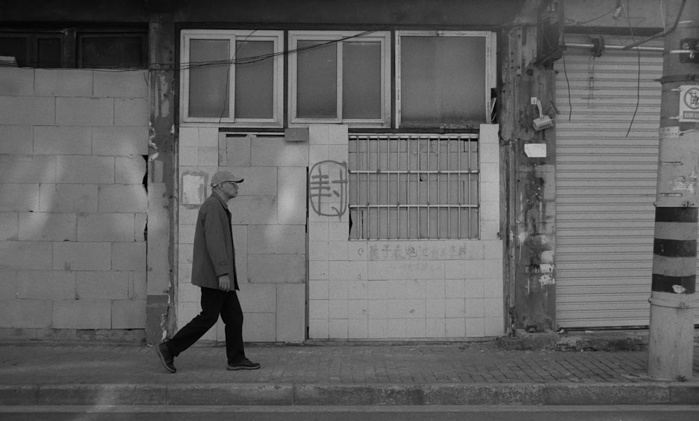 a black and white photo of a man walking past a building