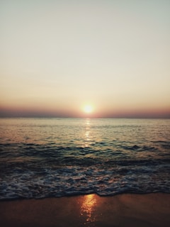 Sunset over a serene tropical beach with gentle waves and a glowing horizon.