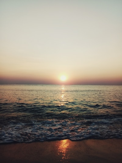 Sunset over a serene tropical beach with gentle waves and a glowing horizon.