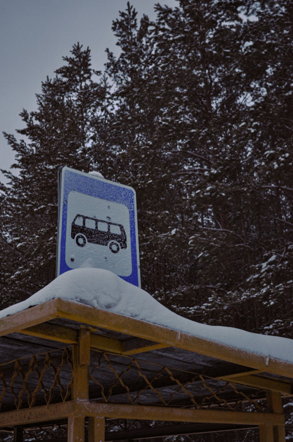 a bus stop sign covered in snow with trees in the background