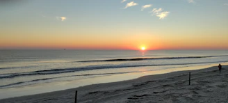 A serene sunrise over a tranquil beach with a lone traveler admiring the view.