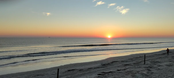 A serene sunrise over a tranquil beach with a lone traveler admiring the view.