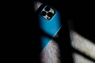 A sleek smartphone with a stylish protective case resting on a dark surface illuminated by soft blue lighting.