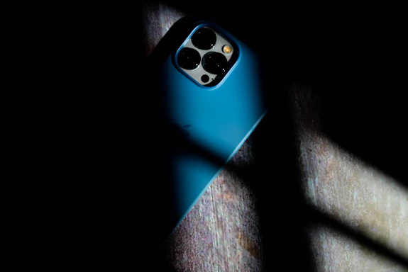 A sleek smartphone with a stylish protective case resting on a dark surface illuminated by soft blue lighting.