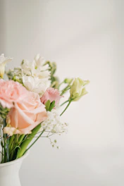 Delicate pastel flowers arranged in a modern glass container against a neutral background.