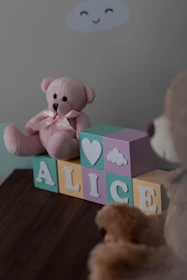 a pink teddy bear sitting on top of a wooden block