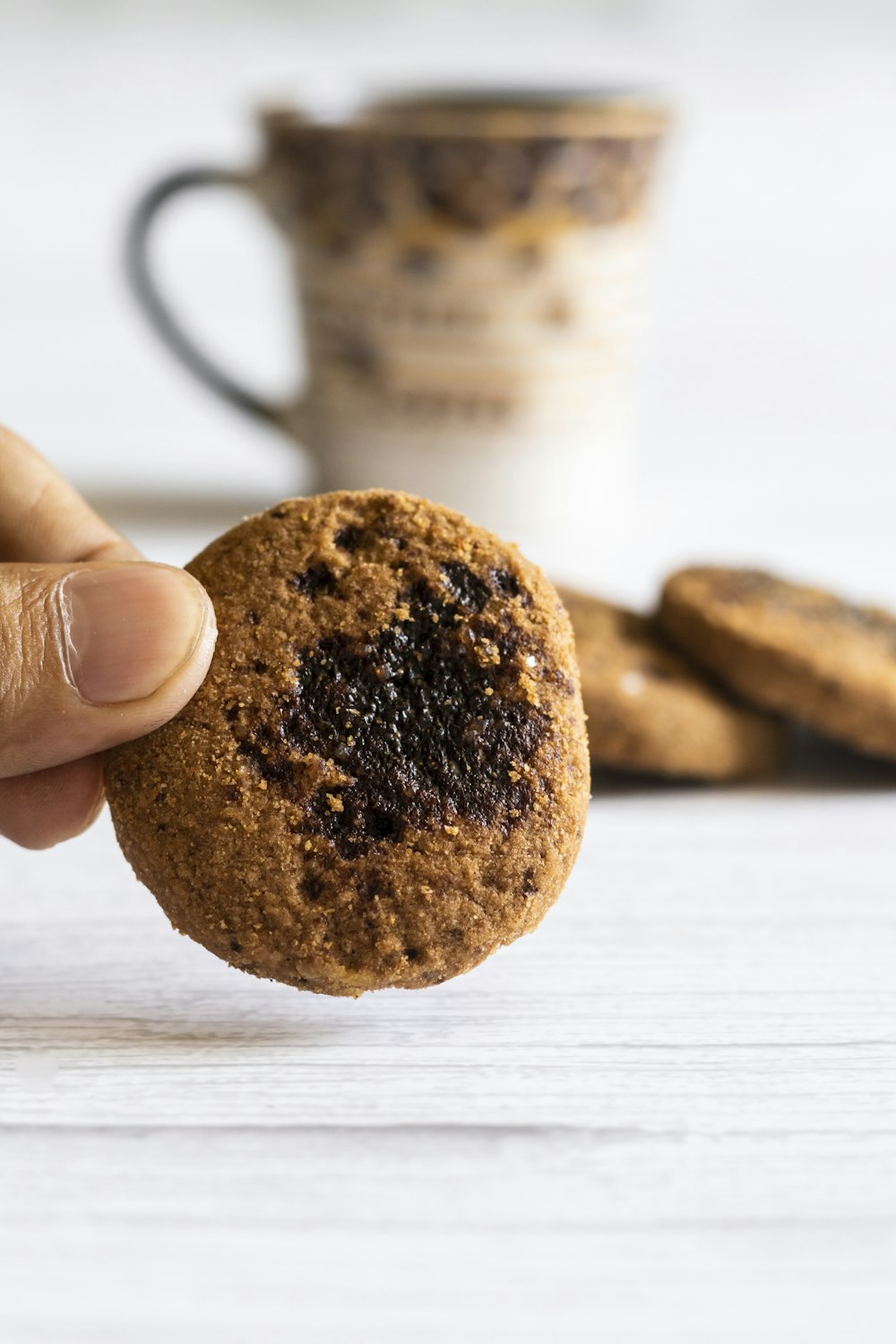 a hand holding a cookie in front of a stack of cookies