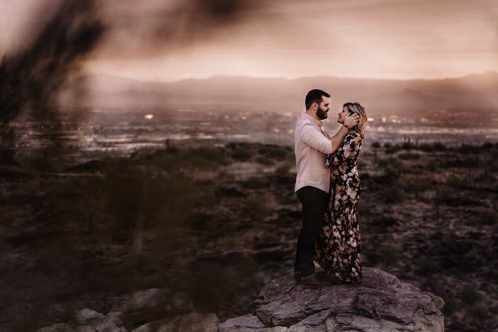 a man and woman standing on top of a rock