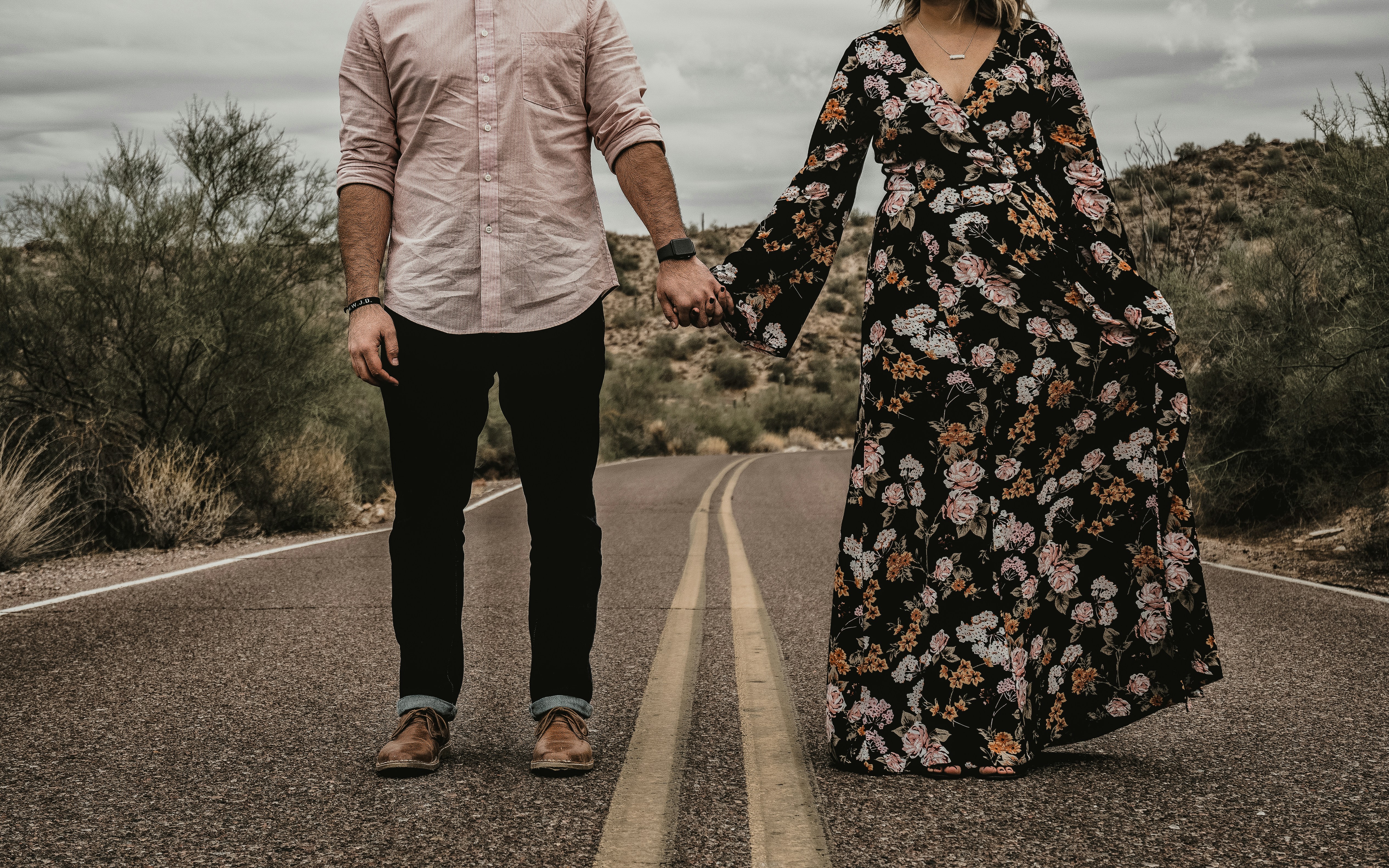 a man and woman holding hands while walking down a road