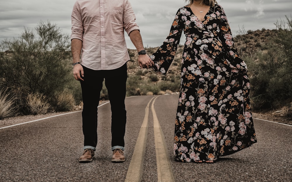 a man and woman holding hands while walking down a road