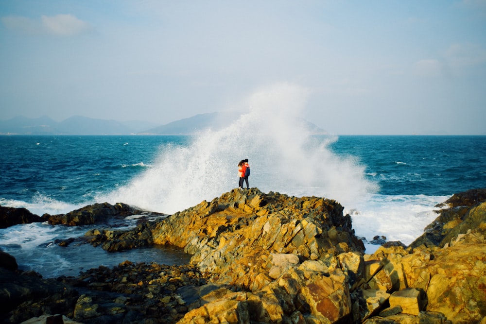 uma pessoa em pé no topo de uma rocha perto do oceano