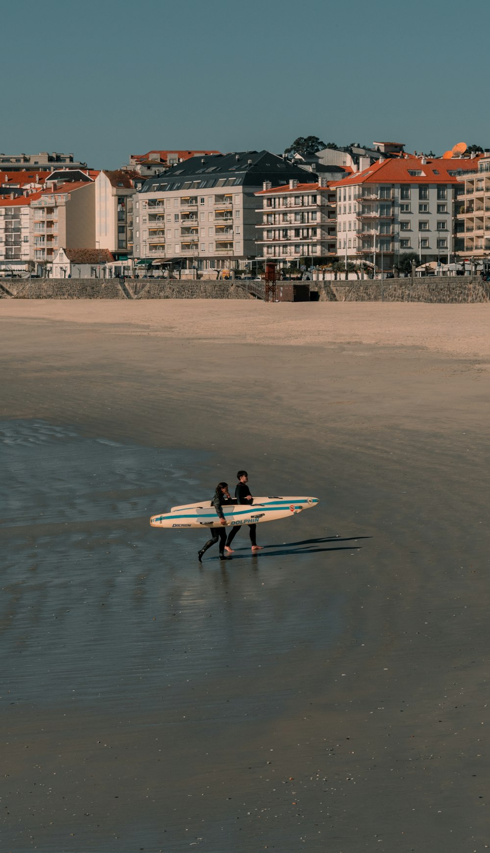 two people walking on the beach with surfboards