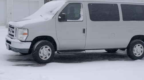 A technician arriving at a snowy driveway with a mobile auto glass repair van.